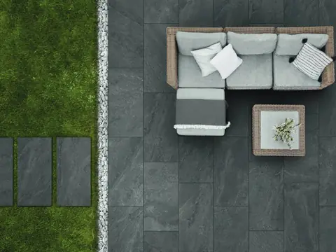Patio con pavimento esterno in gres scuro effetto pietra accanto al prato con lastre a passi